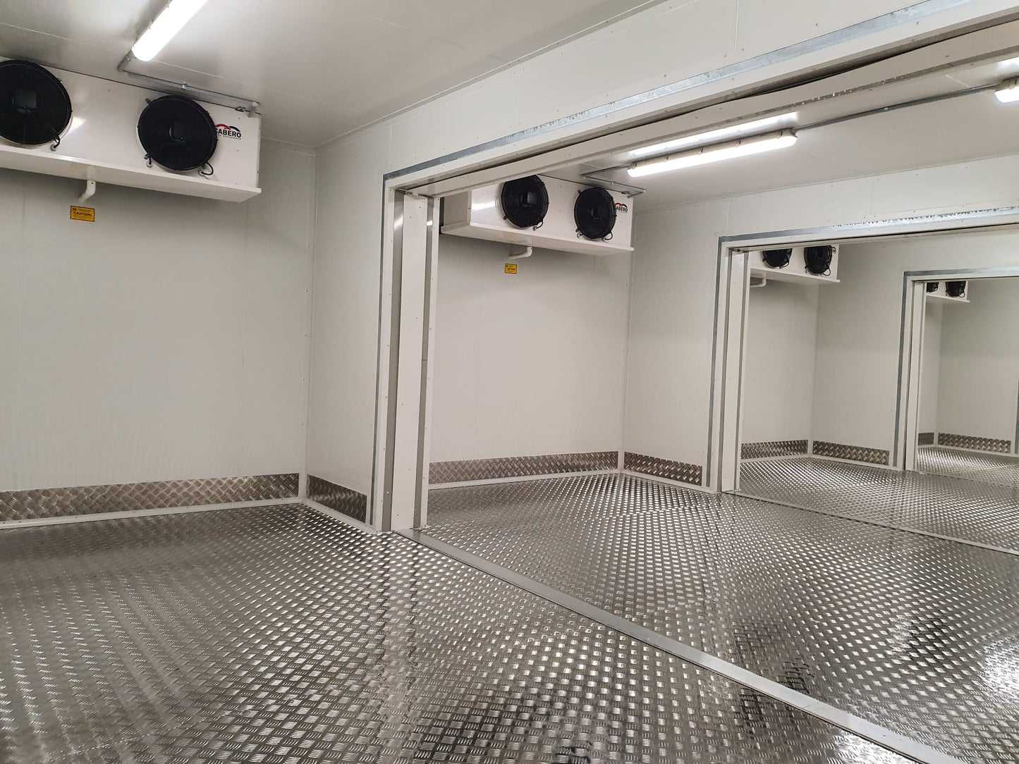 An interior view of a cool room with checker plate flooring, displaying its intricate diamond pattern. The metallic sheen of the checker plate covers the entire floor, reflecting the room's overhead lights.